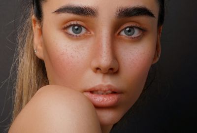 Frau mit dunklen Haaren und nackten Schultern vor dunklem Hintergrund